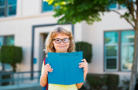 Photo for Smiling little student boy wearing school backpack and holding exercise book. Portrait of happy pupil outside the primary school. Closeup face of smiling hispanic schoolboy looking at camera - Royalty Free Image