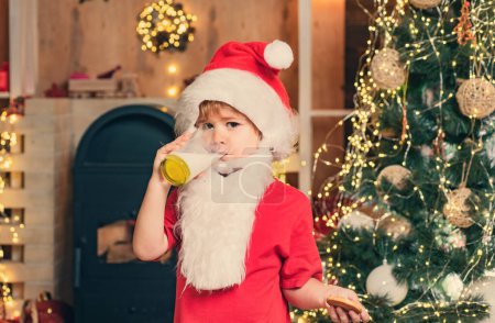 Téléchargez les photos : Le Père Noël aime les biscuits et le lait laissés pour lui la veille de Noël. Portrait de Père Noël surpris et drôle. Biscuit au lait et pain d'épice pour le Père Noël sur fond de lumière de Noël - en image libre de droit