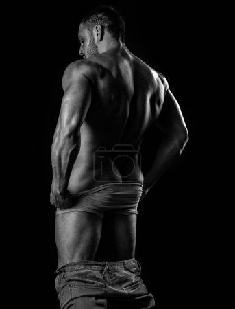 Foto de Musculoso sin camisa modelo masculino mostrando culo en ropa interior gris contra fondo negro estudio aislado - Imagen libre de derechos