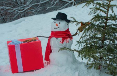 Téléchargez les photos : Bûcheron bonhomme de neige avec hache dans la forêt d'hiver. SnowMan va couper un sapin de Noël. Un bonhomme de neige avec une hache porte un sapin de Noël dans le bois. Bonhomme de neige avec fraîchement coupé arbre de Noël à - en image libre de droit