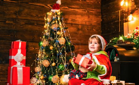 Photo for Christmas gift. Cute little child boy play near christmas tree. Kid enjoy winter holiday at home. Home filled with joy and love. Merry christmas and happy new year. Best wishes. Family holiday. - Royalty Free Image