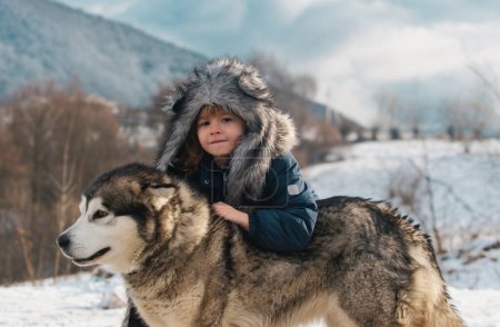Foto de Infancia invernal. El niño abrazó al perro husky. Adorable niño pequeño con perro husky divertirse en el día de invierno - Imagen libre de derechos