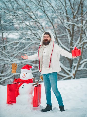 Téléchargez les photos : Père heureux avec cadeau de Noël sur fond de bonhomme de neige d'hiver. Joyeux Noël et bonnes vacances. Noël Homme et bonhomme de neige sur fond de neige blanche - en image libre de droit