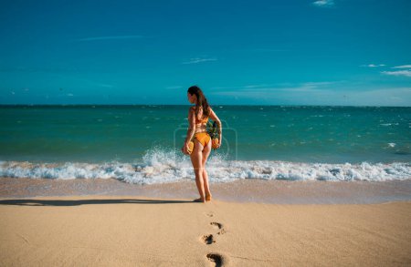 Photo for Beautiful caucasian sunbathed woman model in swimsuit posing on summer beach with white sand on blue sky on virginia or tenerife ocean background. Buttocks, butt, ass with pineapples - Royalty Free Image