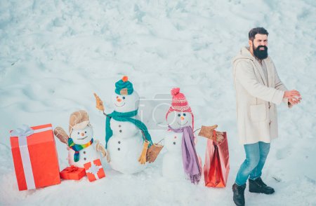 Foto de Feliz Navidad y Feliz Año Nuevo. Preparación de Navidad - hombre barbudo divertido con caja de regalo roja hacer muñeco de nieve - Imagen libre de derechos