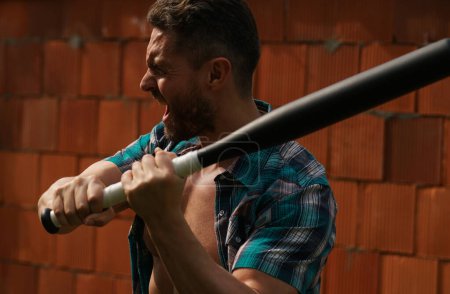 Téléchargez les photos : Portrait d'un bel homme avec une batte de baseball pour le combat. Homme dangereux avec une émotion grave - en image libre de droit