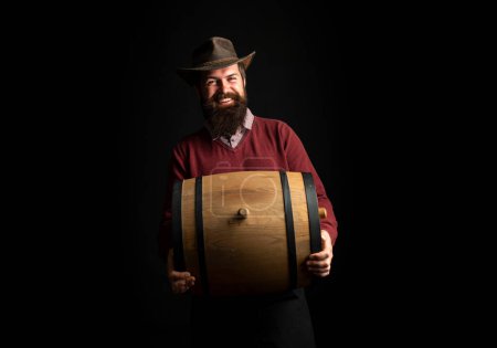 Photo for Man hold wooden barrel on black. Oktoberfest. Bearded brewer man. Serious man . Brewery concept. Beer for pub and bar. Oak barrels, keg. Man carries wooden barrel. Barrel with whiskey, cognac - Royalty Free Image