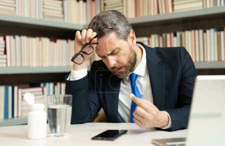 Photo for Sad man got migraine touches her head because of pain. Man manager with strong headache working on laptop. Overworked freelancer or manager at office. Stressed, tired man with headache - Royalty Free Image