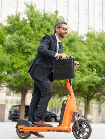 Téléchargez les photos : Homme d'affaires semble cool et à la mode sur son scooter électrique. Écologique et rapide. Beau homme d'affaires en scooter électrique. Réunion d'affaires rapide. Homme d'affaires, temps et argent sur le trajet quotidien - en image libre de droit
