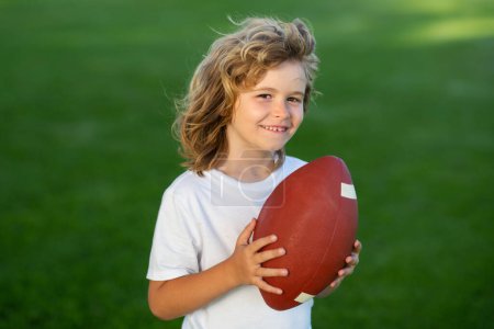 Téléchargez les photos : Enfant sportif. Football, rugby, football américain. Enfant garçon jouer au football extérieur - en image libre de droit