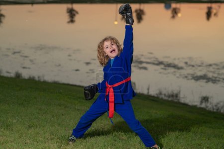 Photo for Kid boy practicing box outdoor. Sport karate kids. Little boy in kimono doing box in park. Child with boxing gloves training box. Little fighter. Martial arts kids. Child in kimono doing boxing punch - Royalty Free Image