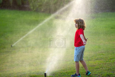 Photo for Child play in summer garden. Grass watering. Automatic sprinkler irrigation system in a green park watering lawn. Sprinkler watering. Child gardening concept. Little kid having fun on water spraying - Royalty Free Image