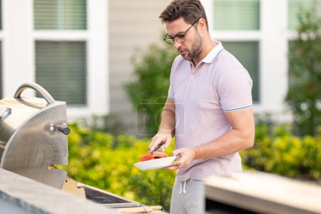 Photo for Barbecue master. Middle aged hispanic man in apron for barbecue. Roasting and grilling. Man hold cooking utensils barbecue. Roasting meat outdoors. Barbecue and grill. Cooking meat in home yard - Royalty Free Image