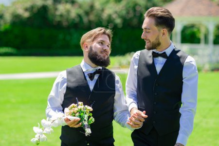 Foto de Los novios gay caminando juntos el día de la boda. Pareja homosexual celebrando su boda. Pareja LBGT en ceremonia de boda - Imagen libre de derechos
