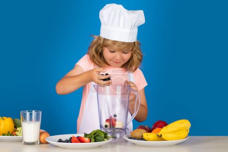 Téléchargez les photos : Cuisiner des enfants. Chef garçon enfant faisant des légumes frais pour une alimentation saine. Portrait de petit enfant en forme de cuisinier isolé sur fond gris. Un petit chef. Processus de cuisson - en image libre de droit