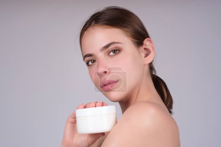 Photo for Beautiful model applying cosmetic cream treatment on face. Facial treatment. Beauty portrait of young topless woman with bare shoulders applying face cream - Royalty Free Image