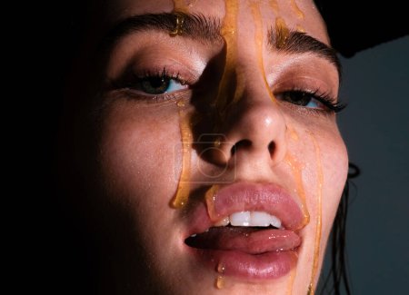 Photo for Portrait of young woman. Beautiful girl tongue licking honey lips. Sensual young woman face with honey drop close up. Sexy model with honey drip on face - Royalty Free Image