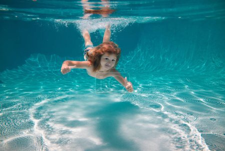 Foto de Niño nadando bajo el agua y sonriendo. Niño feliz nada en la piscina bajo el agua, niño activo nadando bajo el agua, jugando y divirtiéndose, Deportes acuáticos para niños. Vacaciones de verano con niños - Imagen libre de derechos