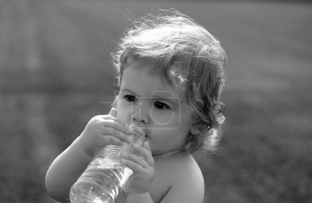 Photo for Baby drinking water. Child drinking water from bottle outdoor on grass background - Royalty Free Image
