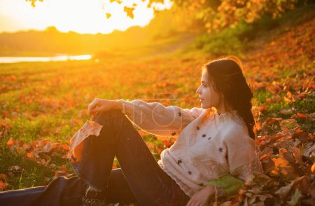 Téléchargez les photos : Profil portrait de belle femme brune au coucher de soleil magnifique soirée automnale. La jeune mère se repose aux feuilles tombées sur le banc de la rivière. Concept de maternité et de nature automnale - en image libre de droit