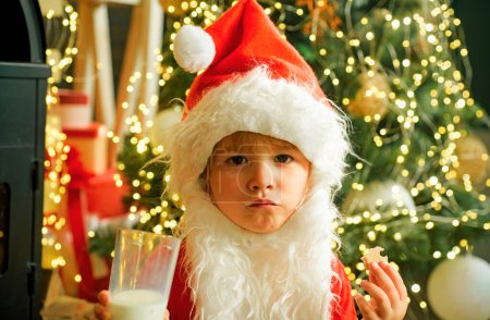Photo for Santa picking cookie and glass of milk at home. Santa child eating cookies and drinking milk. Happy New Year. Greeting card background. Little boy Santa Claus. Cookies for Santa Claus child - Royalty Free Image
