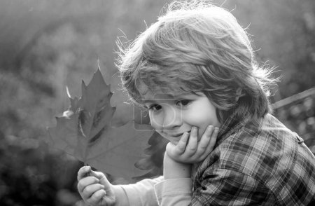 Téléchargez les photos : Adorable petit garçon avec des feuilles d'automne dans le parc de beauté. Les enfants rêvent - en image libre de droit