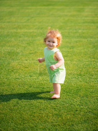 Téléchargez les photos : Joyeux bébé dans l'herbe sur le fieald le soir d'été. Souriant enfant à l'extérieur - en image libre de droit
