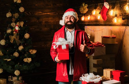 Foto de Hombre de Navidad en vestido rojo de moda. Bearded santa moderna desea Feliz Navidad y Feliz año nuevo. Santa Claus con caja de regalo roja de Navidad - Imagen libre de derechos