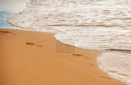 Photo for Footprints at golden sand, footsteps. Sea background, nature of tropical summer beach with rays of sun light. Sand beach, sea water with copy space, summer vacation concept - Royalty Free Image