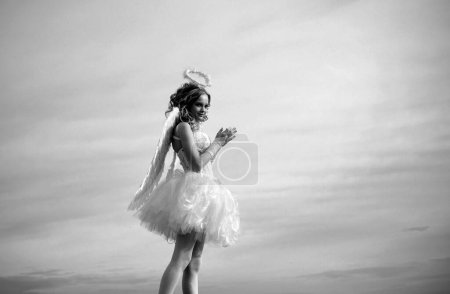 Téléchargez les photos : Charmante petite fille bouclée en robe blanche et ailes ange fille Cupidon. Profiter d'un moment magique. Cupidon chérubin adolescent. Ciel - en image libre de droit