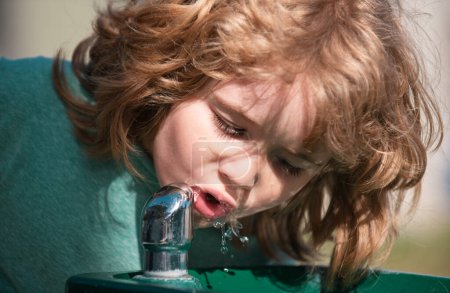 Téléchargez les photos : Portrait d'enfant caucasien buvant de l'eau en plein air dans le parc. Enfants dans le parc naturel d'été. Enfants assoiffés - en image libre de droit