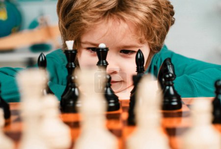 Foto de Un chico listo pensando en ajedrez. Desarrollo temprano de los niños. Hijo están jugando ajedrez y sonriendo en casa. Retrato de cerca, cara divertida - Imagen libre de derechos