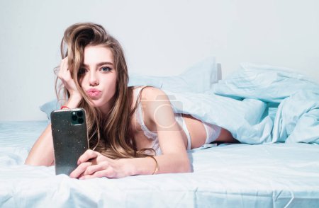 Photo for Sexy beautiful woman with a smartphone in bed. Beautiful sensual girl making selfie with her cell phone in her bedroom - Royalty Free Image