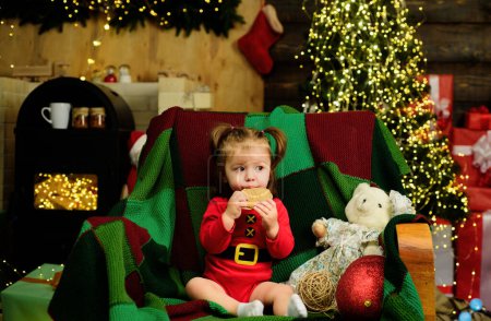 Téléchargez les photos : Mignon visage de bébé dans le chapeau de Père Noël près de l'arbre de Noël. Joyeux Enfance. Nouvel an enfants - en image libre de droit