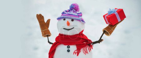 Téléchargez les photos : Bonhomme de neige avec une écharpe et un chapeau tricoté. Mignons bonhommes de neige debout en arrière-plan d'hiver. Salut bonhomme de neige - en image libre de droit