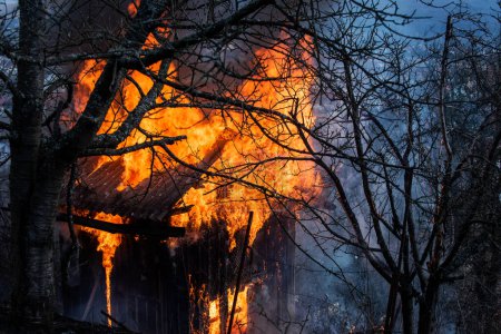 Téléchargez les photos : Une maison en bois en feu. Une flamme de feu flamboyante. Un incendie. Bâtiment en feu. Ouvrez les flammes. Feu dans la maison - en image libre de droit