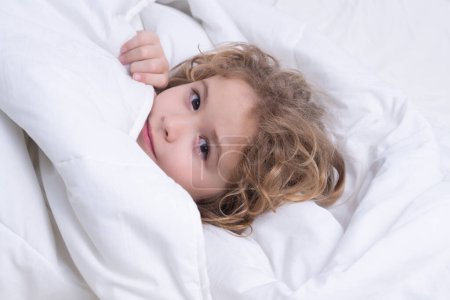 Photo for Kid under covers, face cover with blanket. Kid in bed with comfortable mattress soft pillow white bedding. Kid wake up cover blanket. Good morning - Royalty Free Image