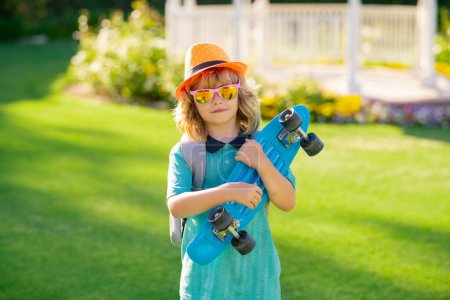 Photo for Child with skateboard on summer backyard. Funny kid boy, stylish skater holding skateboard outdoor. Concept of activity and happy childhood - Royalty Free Image