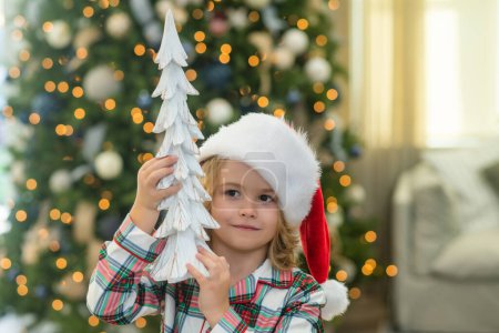 Foto de Niño feliz en sombrero de santa cerca del árbol de Navidad en casa - Imagen libre de derechos