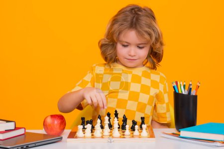 Téléchargez les photos : Les enfants jouent aux échecs en studio. Un gamin joue aux échecs. Enfant pensant. Jeu d'échecs pour les enfants. Intelligent, intelligent et intelligent garçon d'école - en image libre de droit