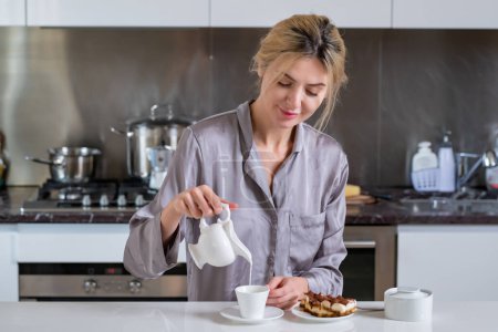 Foto de Ama de casa vertiendo leche en el café y el café en la cocina. Mujer en la cocina por la mañana - Imagen libre de derechos