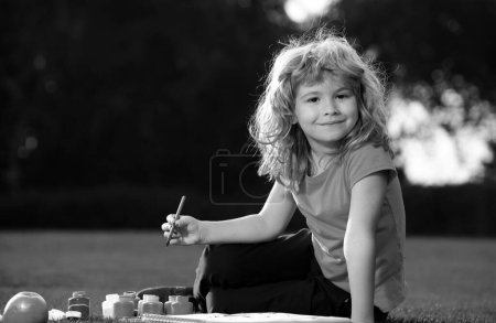 Téléchargez les photos : Enfant garçon peinture dans la nature printanière. Des écoliers dessinent dans un parc d'été, peignent de l'art. Petit peintre dessiner des images en plein air - en image libre de droit