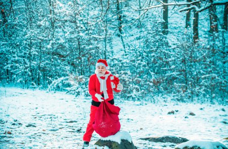 Foto de Santa lleva saco de regalos contra escena de nieve. Santa en el campo de invierno. Santa Claus con una bolsa enorme. Feliz Navidad y felices fiestas - Imagen libre de derechos