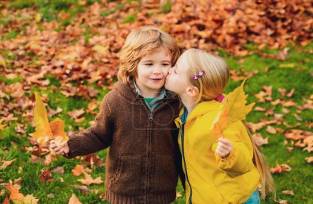 Photo for Playful little cute couple boy and girl walk on autumn park, have fun, kiss, enjoy good sunny day - Royalty Free Image
