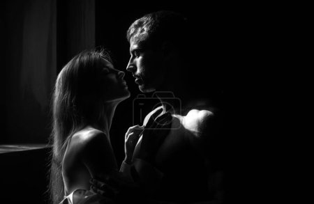 Photo for Man embracing and going to kiss sensual woman. Loving couple kissing in bedroom over black background. Real love on Valentines Day - Royalty Free Image