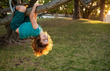 Téléchargez les photos : Jeune garçon jouant et grimpant à un arbre et accrochant à l'envers. adolescent garçon jouer dans un parc - en image libre de droit