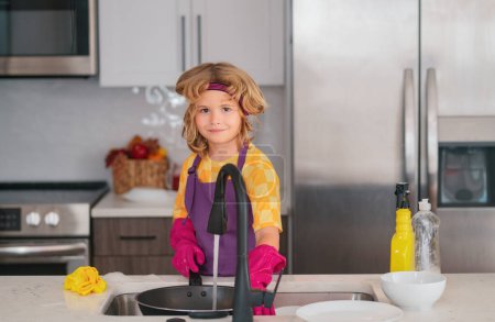 Téléchargez les photos : Adorable petite assistante ménagère pour enfants. Petit garçon mignon balayant et nettoyant la vaisselle à la cuisine - en image libre de droit