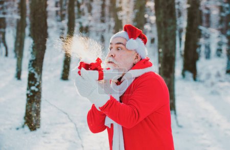 Photo for Santa Claus blowing magic snow of his hands. Portrait of happy Santa Claus walking in snowy forest and Blowing Magic Christmas snow - Royalty Free Image