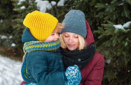Foto de Madre e hijo disfrutando del invierno al aire libre. Pinos cubiertos de nieve. Una hermosa familia camina a través del bosque nevado de invierno. Vacaciones, Navidad, felicidad juntos, infancia enamorada - Imagen libre de derechos