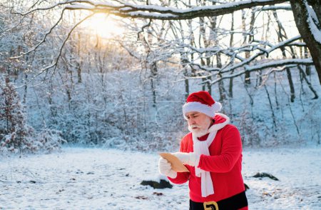 Foto de Santa Claus con la lista de deseos de Navidad viene en el bosque de nieve - Imagen libre de derechos